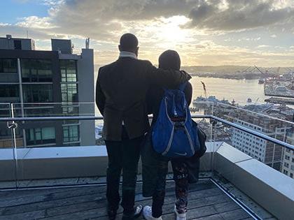 一名学生和一名成人站在西雅图市中心一座建筑物的楼顶上看日落.